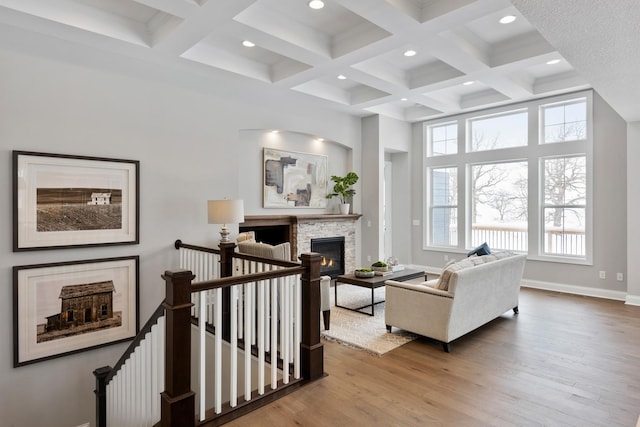 living room with hardwood / wood-style flooring, a stone fireplace, coffered ceiling, and beam ceiling