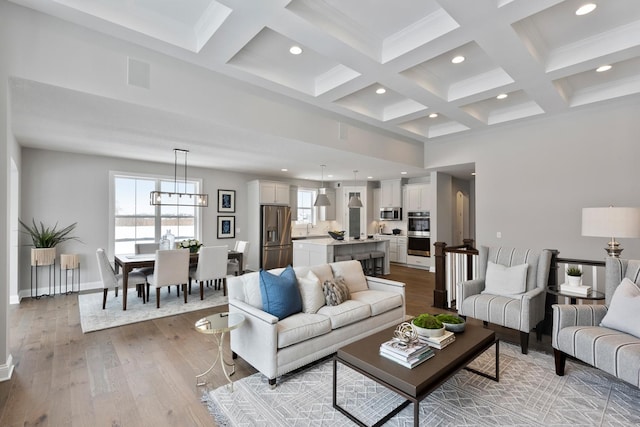 living room with coffered ceiling, sink, light wood-type flooring, a notable chandelier, and beam ceiling