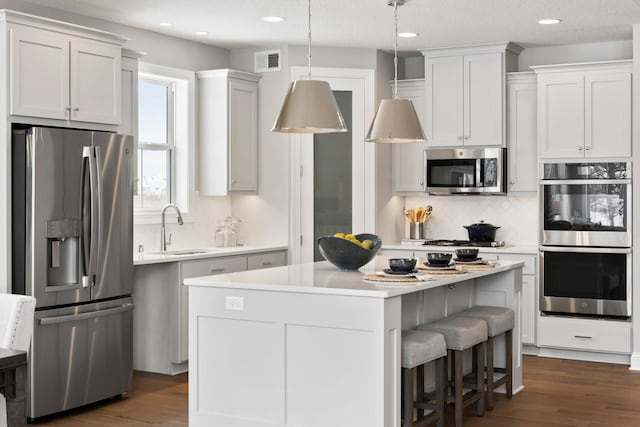 kitchen with pendant lighting, sink, white cabinets, a center island, and stainless steel appliances