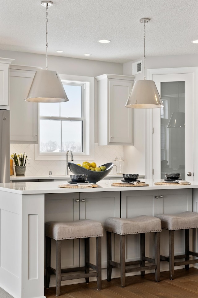 kitchen with white cabinetry, hanging light fixtures, dark wood-type flooring, and a kitchen breakfast bar