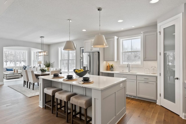 kitchen featuring sink, hanging light fixtures, backsplash, a center island, and stainless steel refrigerator with ice dispenser