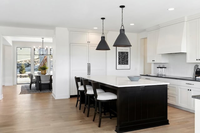 kitchen with custom range hood, pendant lighting, white cabinets, a center island, and light hardwood / wood-style floors