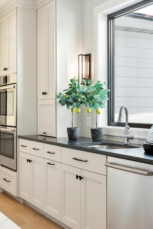 kitchen featuring white cabinets, dishwasher, sink, and double oven