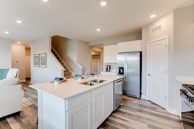 kitchen with a center island with sink, sink, light wood-type flooring, white cabinetry, and stainless steel appliances