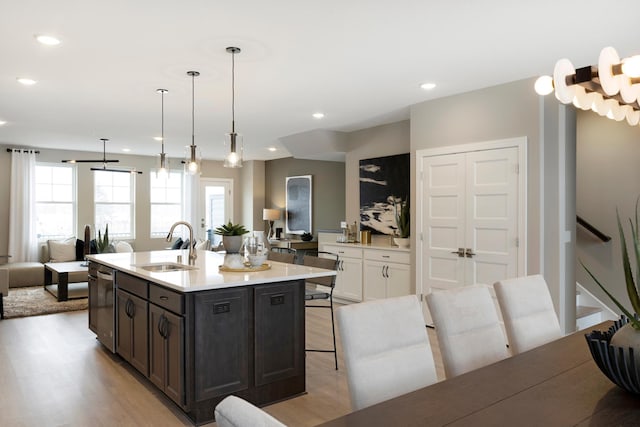 kitchen with sink, light hardwood / wood-style flooring, an island with sink, decorative light fixtures, and white cabinets