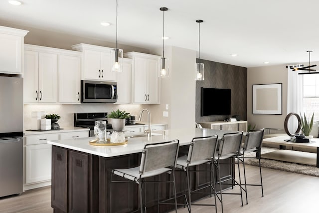 kitchen featuring stainless steel appliances, a kitchen island with sink, light hardwood / wood-style flooring, white cabinetry, and hanging light fixtures