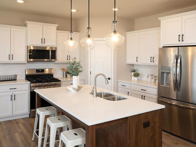 kitchen with a kitchen island with sink, hanging light fixtures, sink, white cabinetry, and stainless steel appliances