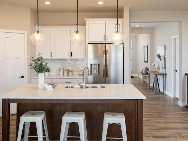 kitchen with a breakfast bar, a kitchen island with sink, sink, stainless steel fridge, and dark hardwood / wood-style flooring