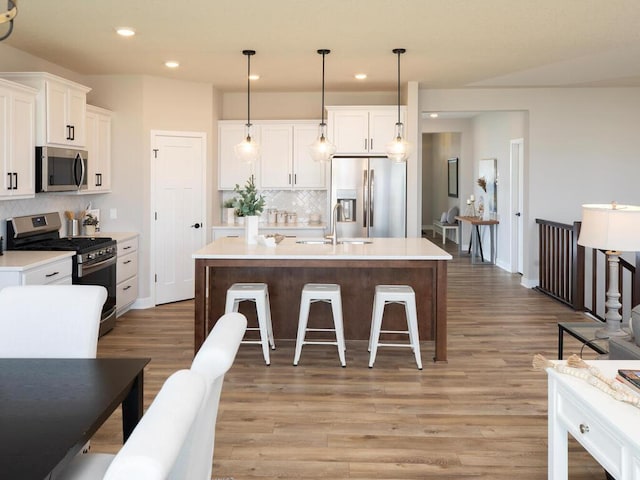 kitchen featuring light hardwood / wood-style flooring, an island with sink, appliances with stainless steel finishes, decorative light fixtures, and white cabinetry