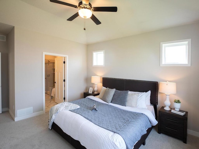 bedroom with light carpet, connected bathroom, multiple windows, and ceiling fan