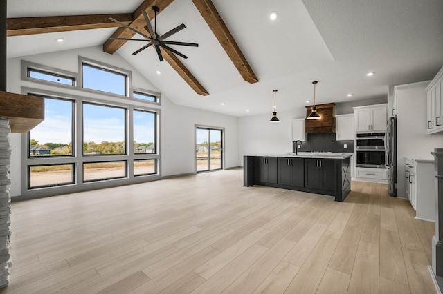 kitchen with white cabinetry, stainless steel appliances, hanging light fixtures, light hardwood / wood-style flooring, and an island with sink