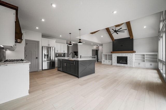 kitchen with a fireplace, light countertops, lofted ceiling with beams, appliances with stainless steel finishes, and ceiling fan