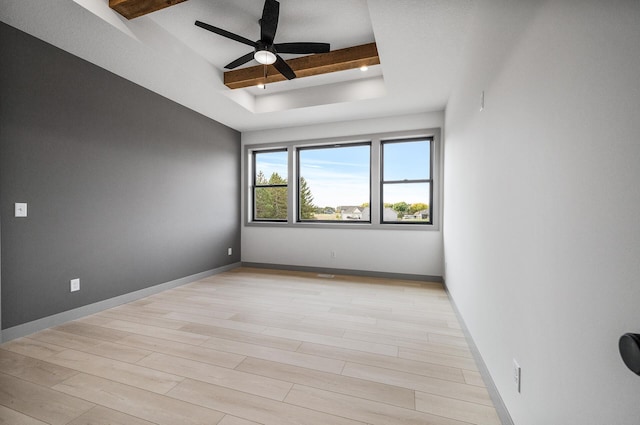 unfurnished room featuring baseboards, a raised ceiling, ceiling fan, light wood-type flooring, and beam ceiling