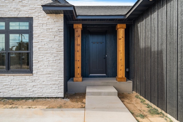 doorway to property featuring stone siding and roof with shingles