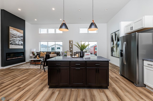 kitchen featuring stainless steel refrigerator with ice dispenser, light wood-type flooring, a large fireplace, pendant lighting, and white cabinets