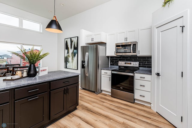 kitchen with white cabinetry, dark stone countertops, pendant lighting, appliances with stainless steel finishes, and light wood-type flooring