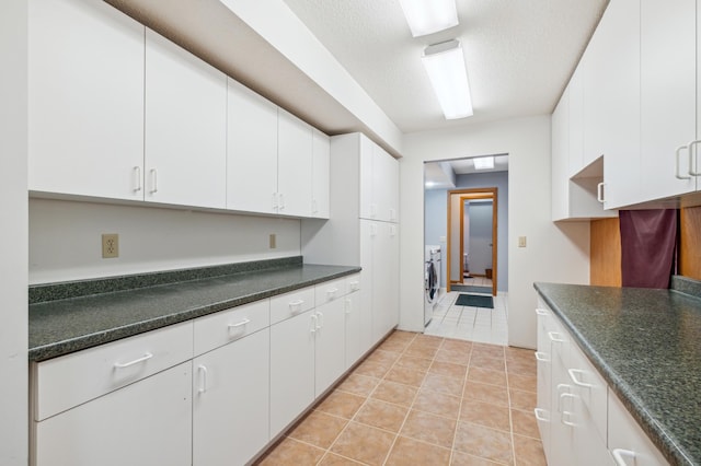 kitchen with white cabinetry, light tile patterned floors, a textured ceiling, and washer / dryer