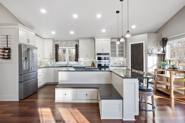 kitchen with appliances with stainless steel finishes, a kitchen island, sink, white cabinetry, and hanging light fixtures