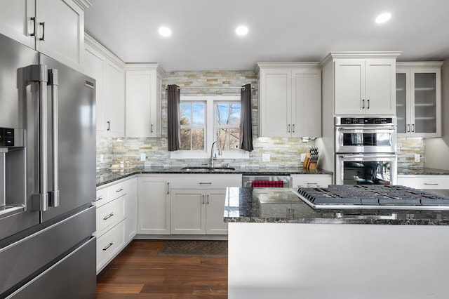 kitchen with appliances with stainless steel finishes, white cabinetry, dark stone counters, and sink