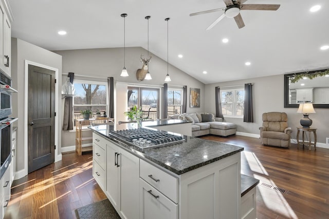 kitchen featuring dark stone counters, stainless steel gas stovetop, ceiling fan, white cabinetry, and hanging light fixtures