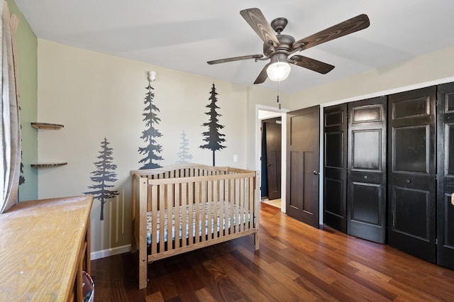 bedroom with ceiling fan, dark hardwood / wood-style flooring, a crib, and a closet