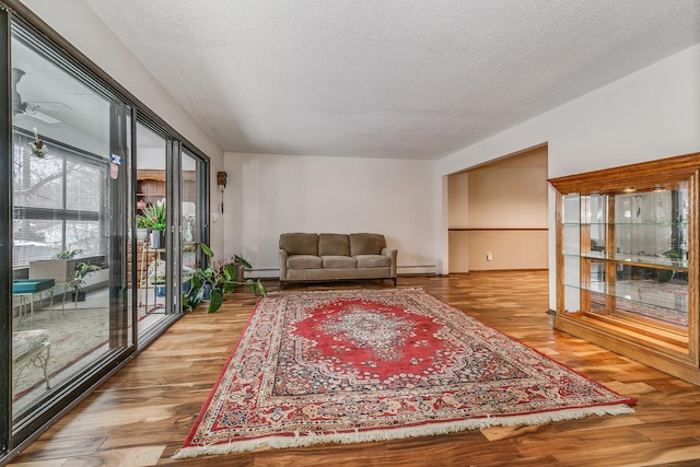 living room with ceiling fan, baseboard heating, a textured ceiling, and light hardwood / wood-style floors