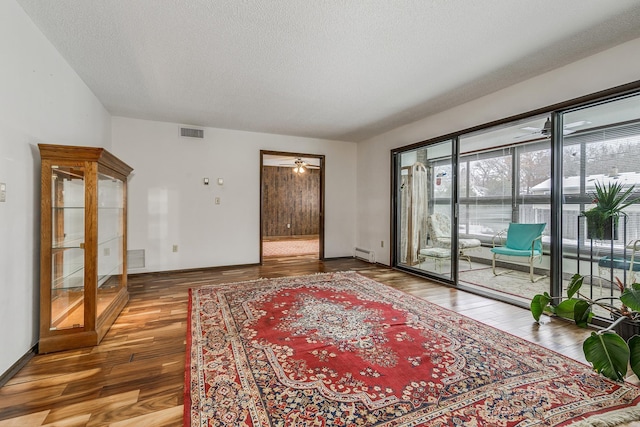 interior space with a baseboard heating unit, ceiling fan, a textured ceiling, and hardwood / wood-style flooring