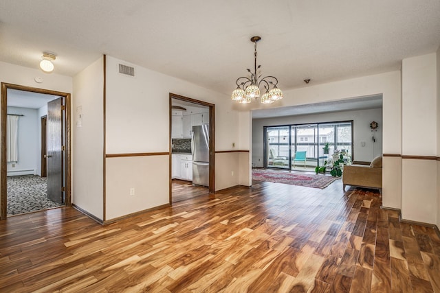 unfurnished dining area featuring a textured ceiling, a chandelier, hardwood / wood-style floors, and a baseboard radiator