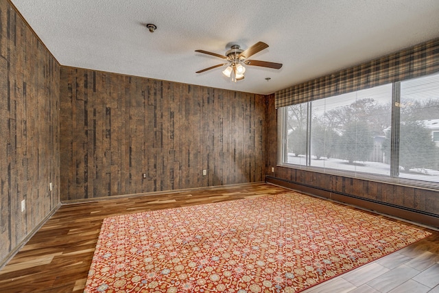 unfurnished room featuring a textured ceiling, ceiling fan, wood-type flooring, and wood walls