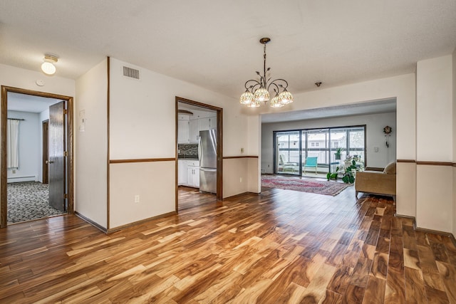 unfurnished dining area featuring wood finished floors, a chandelier, and a baseboard heating unit