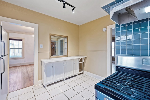 kitchen with white refrigerator, light tile patterned floors, range hood, white cabinetry, and range