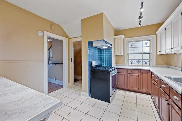 kitchen with rail lighting, stainless steel range with gas cooktop, light tile patterned flooring, lofted ceiling, and white cabinets