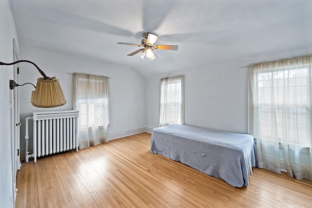 bedroom with multiple windows, light hardwood / wood-style floors, radiator, and ceiling fan