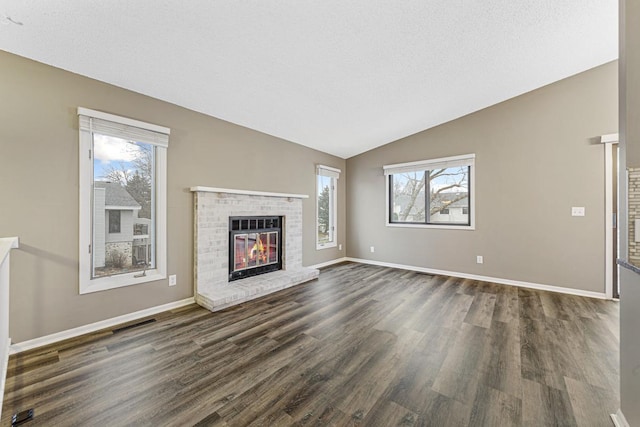 unfurnished living room featuring dark hardwood / wood-style flooring, plenty of natural light, lofted ceiling, and a brick fireplace