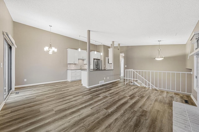 unfurnished living room with sink, a brick fireplace, a chandelier, a textured ceiling, and hardwood / wood-style flooring