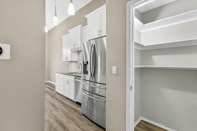 kitchen with appliances with stainless steel finishes, hardwood / wood-style flooring, white cabinetry, and hanging light fixtures