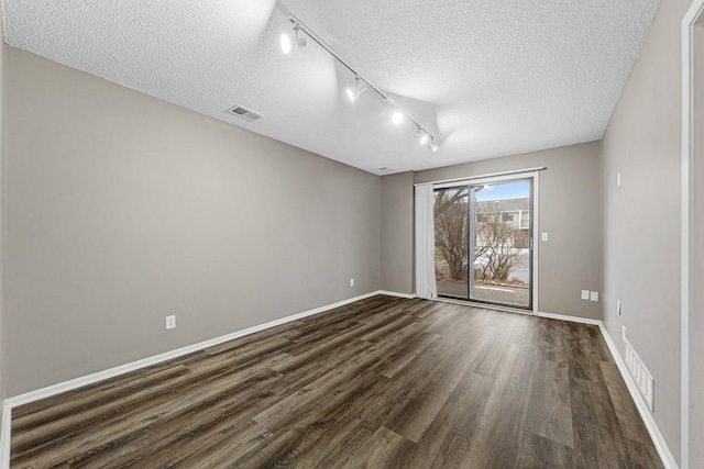 empty room featuring a textured ceiling, dark hardwood / wood-style flooring, and rail lighting