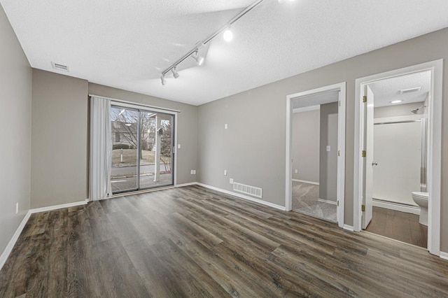 unfurnished room with a textured ceiling, rail lighting, baseboard heating, and dark wood-type flooring