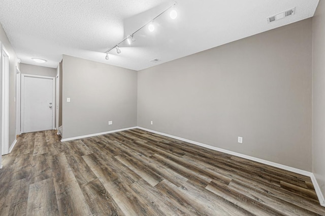 empty room with track lighting, dark wood-type flooring, and a textured ceiling