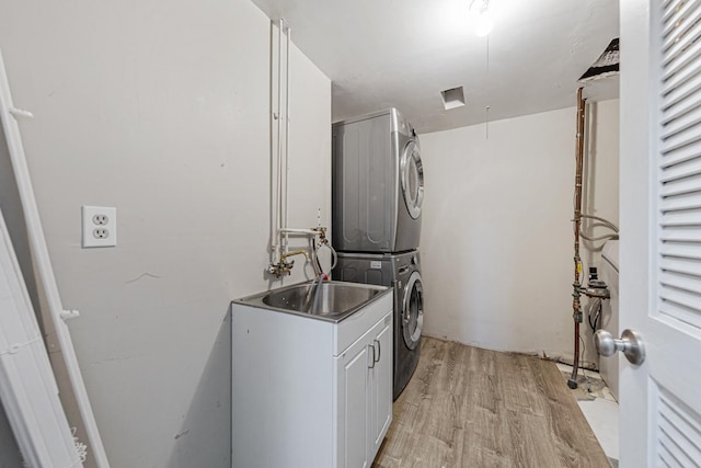 laundry room with stacked washer / dryer, sink, cabinets, and light wood-type flooring