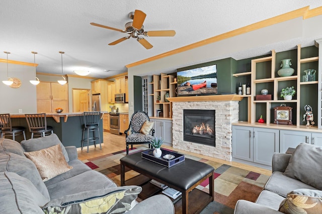 living room featuring crown molding, a textured ceiling, ceiling fan, and a fireplace