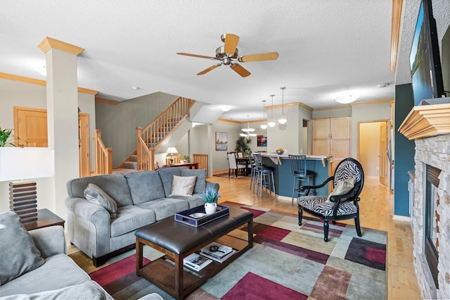 living area with ornamental molding, stairs, a fireplace, light wood-style floors, and a ceiling fan