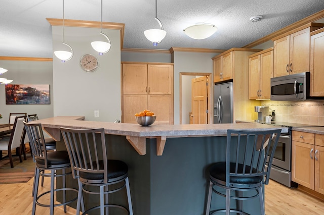 kitchen with light brown cabinetry, appliances with stainless steel finishes, ornamental molding, and a kitchen bar