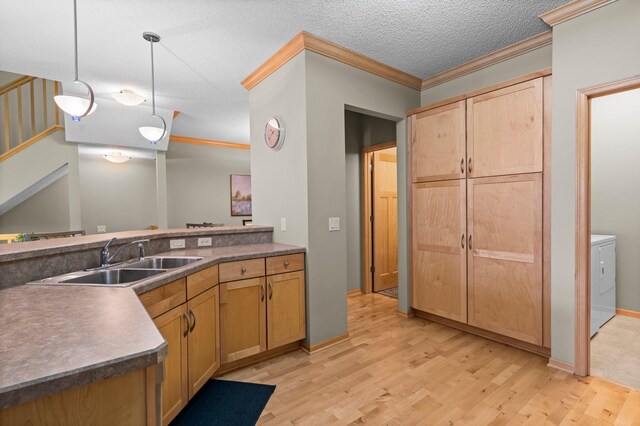 kitchen with decorative light fixtures, a sink, light wood finished floors, washer / dryer, and ornamental molding