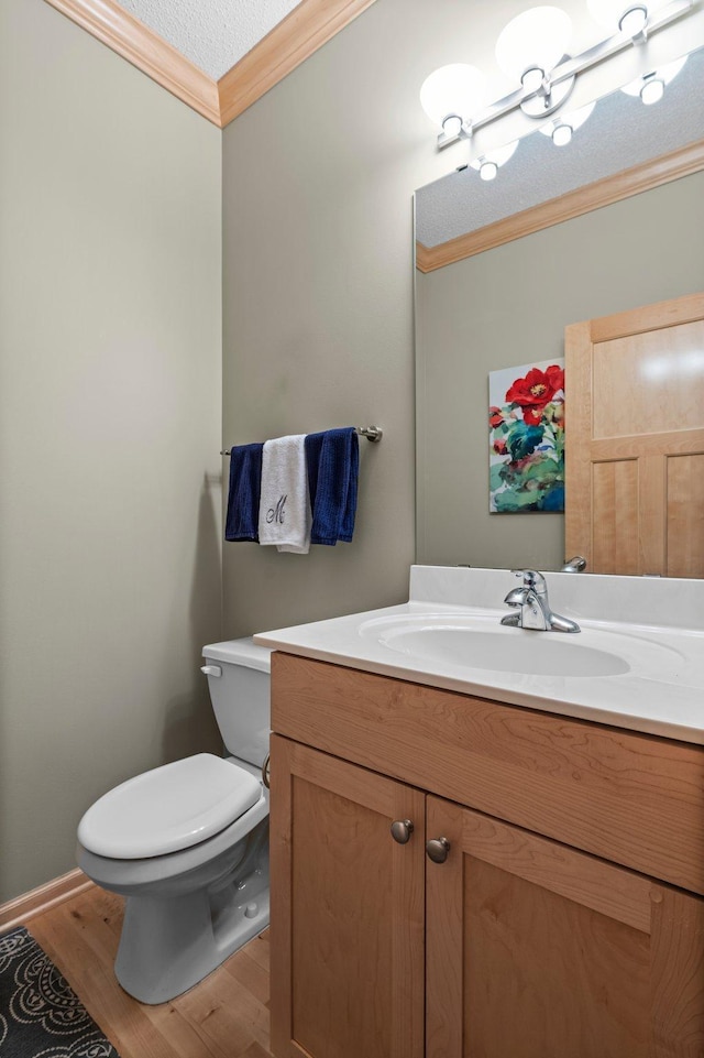 half bath featuring wood finished floors, vanity, baseboards, toilet, and ornamental molding