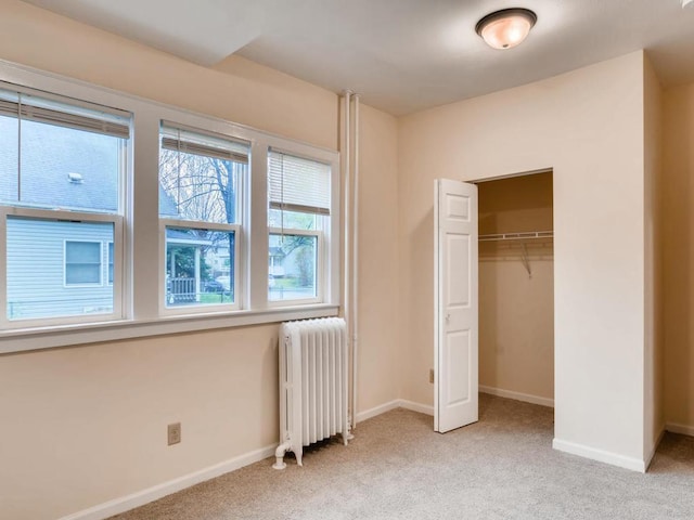 unfurnished bedroom with radiator heating unit, light carpet, and a closet