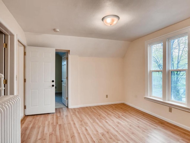 additional living space featuring lofted ceiling, radiator heating unit, and light hardwood / wood-style flooring