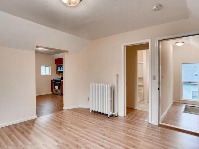 unfurnished room with a wealth of natural light, light wood-type flooring, and radiator