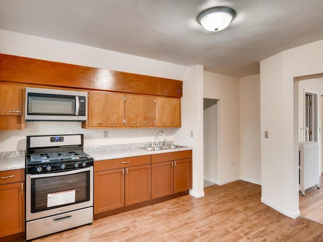 kitchen with sink, light wood-type flooring, a textured ceiling, appliances with stainless steel finishes, and radiator heating unit