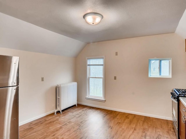 bonus room featuring radiator heating unit, a textured ceiling, light hardwood / wood-style flooring, and lofted ceiling